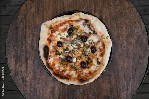 Traditional pizza. Top view of a mozzarella cheese pizza with tomato sauce, black olives and fresh oregano, on the wooden table.