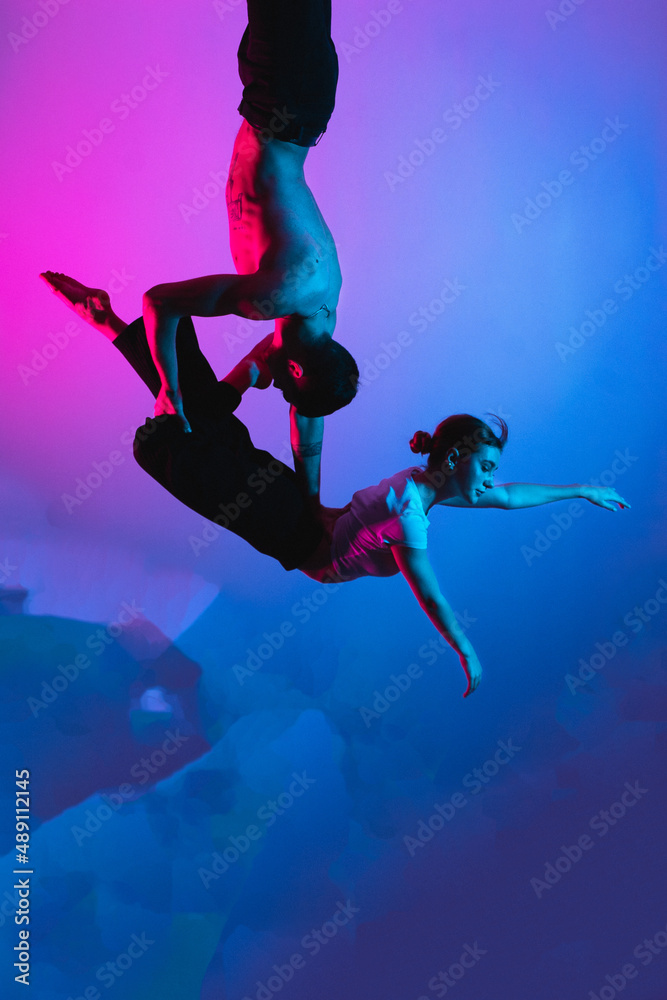Gymnastics support. A man with a girl perform an acrobatic exercise, neon light Gymnastics support. A man with a girl perform an acrobatic exercise, neon light