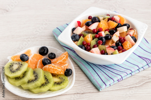 In a white bowl  fresh fruit sliced salad with apple  grapes  tangerine  kiwi  cranberries and blueberries. For a healthy diet.