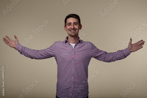 Portrait of young happy laughing man which celebrating with hands raised to the sides. Successful happy man in casual shirt.