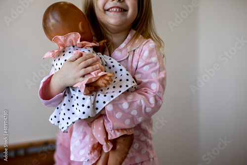 Little dark-haired girl in pink pajamas lies on a cozy soft bed. Good morning.