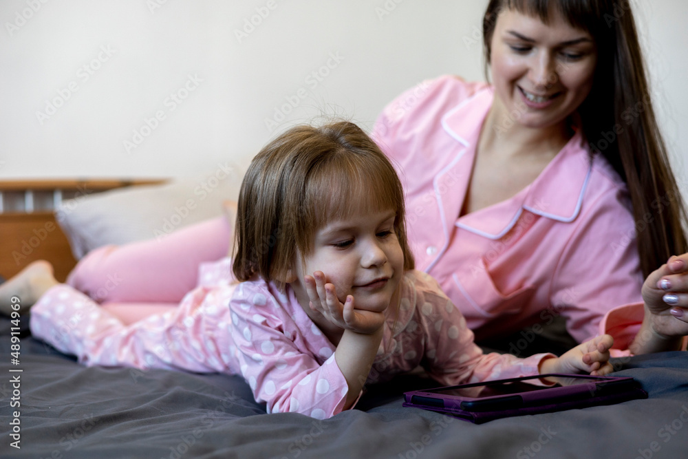 Mother and her child are watching on screen of digital tablet pc lying on the bed. Mother and her child are watching on screen of digital tablet pc lying on the bed.