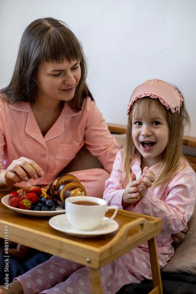 Beautiful young woman with a little cute girl spend time together at home, sitting on the bed. Beautiful young woman with a little cute girl spend time together at home, sitting on the bed.