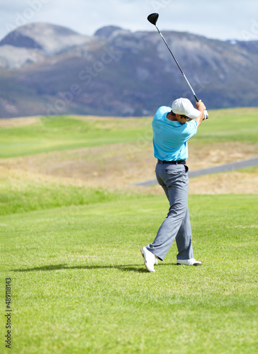 Driving it down the fairway. A young, fit male golfer following through after driving his ball down the fairway.