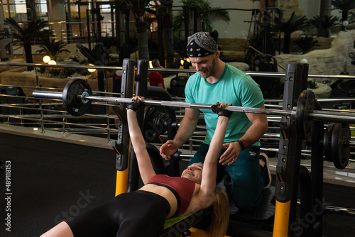 Instructor led training helps a beautiful client to perform exercises in a fitness club, the concept of playing sports with a professional gym leisure lifestyle male modern, in the afternoon