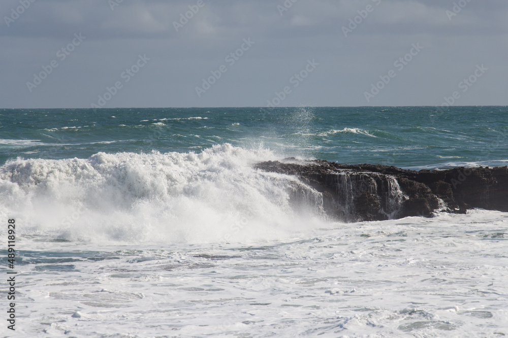 Waves are crashing on a group of stones.