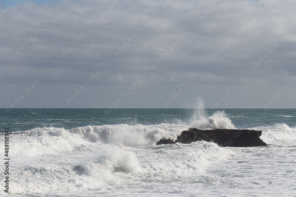 Waves are crashing on a group of stones.