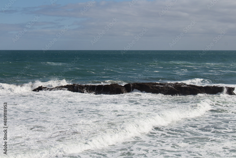 Waves are crashing on a group of stones.