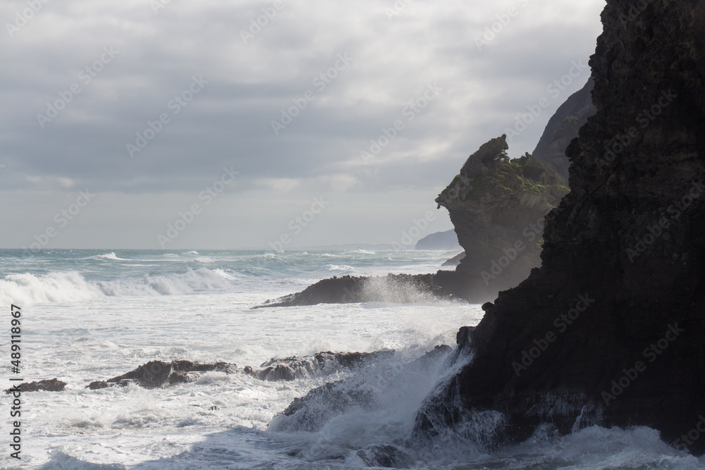 Marine landscape with an inclined rock, waves and cloudy sky on background, West Beach near Auckland, New Zealand.