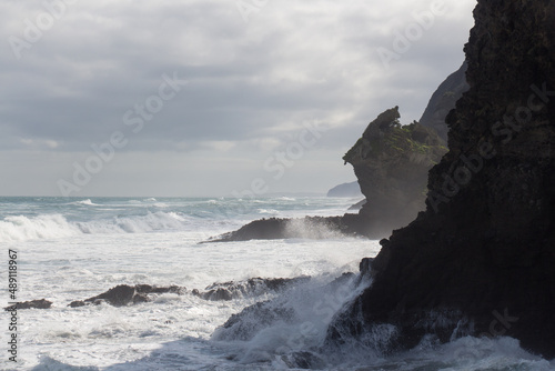 Marine landscape with an inclined rock, waves and cloudy sky on background, West Beach near Auckland, New Zealand.