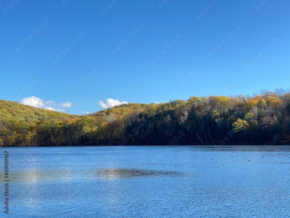 Paysage d'une montagne avec des arbres en couleurs qui se découpe sur un ciel bleu presque sans nuage et une belle étendue d'eau. Lac et collines en automne
