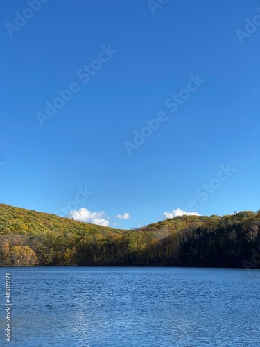 Paysage d'une montagne avec des arbres en couleurs qui se découpe sur un ciel bleu presque sans nuage et une belle étendue d'eau. Lac et collines en automne, panorama pittoresque