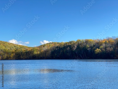 Paysage d'une montagne avec des arbres en couleurs qui se découpe sur un ciel bleu presque sans nuage et une belle étendue d'eau. Lac et collines en automne