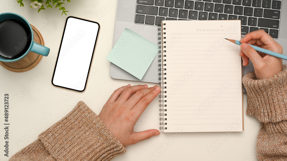 Top view, Female in comfy sweater writing her diary in minimal workspace. Top view, Female in comfy sweater writing her diary in minimal workspace.