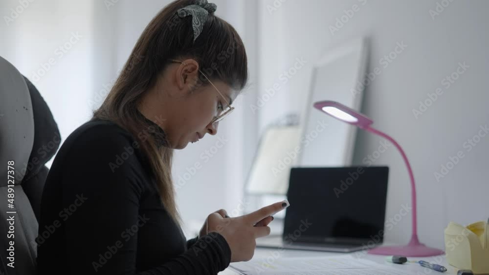 A young student of Colombian universitary typing text in her phone then she puts down the phone and goes back to study. A young student of Colombian universitary typing text in her phone then she puts down the phone and goes back to study.