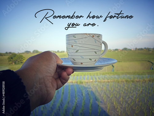 Inspirational motivational words - Remember how fortune you are. With person holding cup of coffee in hand on background of bright green paddy field view in the morning. Grateful concept. photo