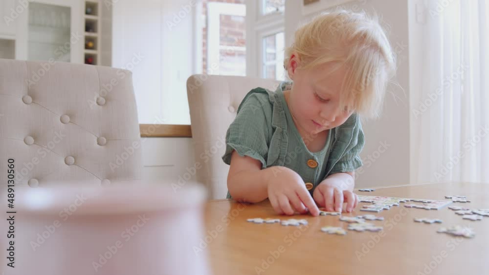 Young girl having fun sitting at table at home doing jigsaw puzzle - shot in slow motion Young girl having fun sitting at table at home doing jigsaw puzzle - shot in slow motion