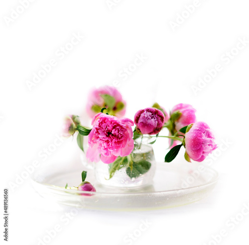 Pink peonies in a glass on table, white blurred background. Bouquet of spring flowers. Beautiful floral still life with pink peonies