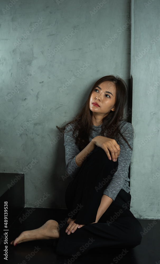Fototapeta premium Young woman sitting sad at wall, depression emotion, looking above space in dark room, Portrait of young beautiful woman or female or girl sitting expression depression emotional alone