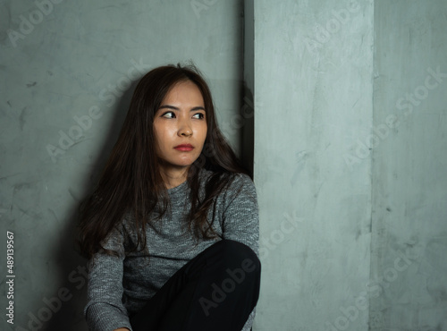 Young woman sitting sad against wall, depression emotion, looking above space in dark room, Portrait of young beautiful woman or female or girl sitting expression depression emotional alone