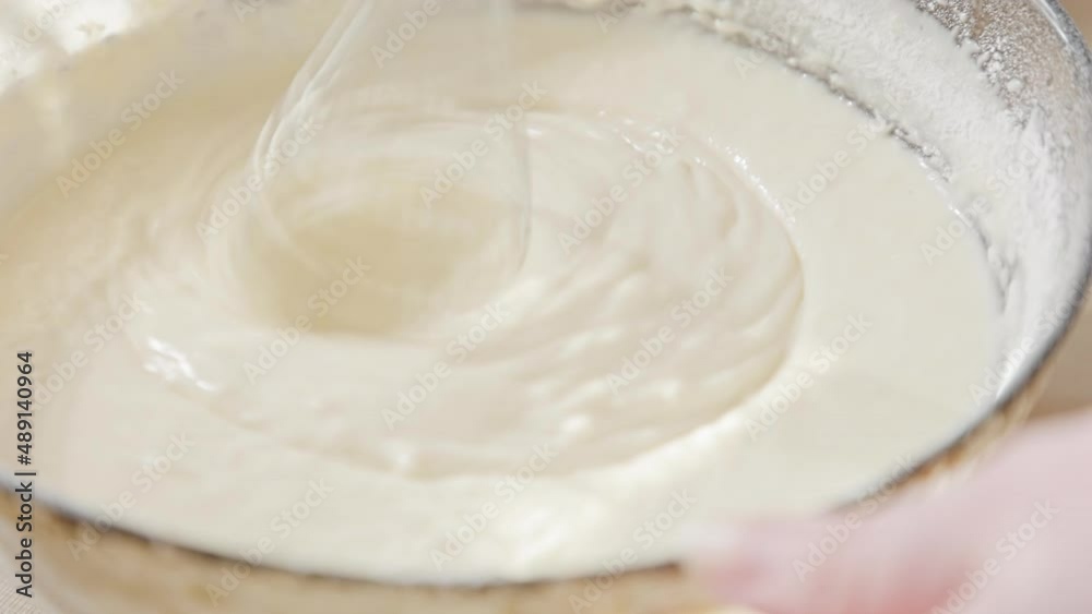 Person slowly mix dough with a blender in a glass bowl. Close up. Cooking comfort food concept. Person slowly mix dough with a blender in a glass bowl. Close up. Cooking comfort food concept.