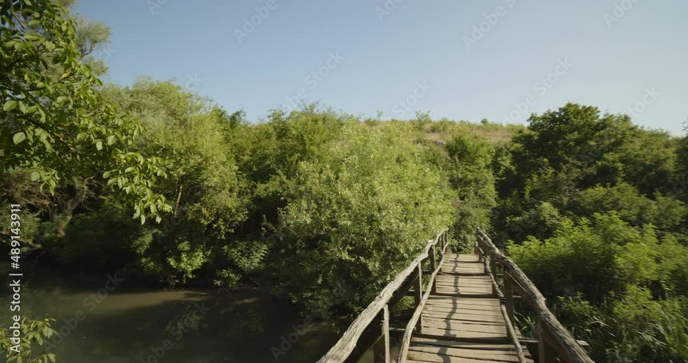 POV shot, crossing a bridge over a quiet river with green trees and bushes around it. Iskar-Panega eco trail, Bulgaria. POV shot, crossing a bridge over a quiet river with green trees and bushes around it. Iskar-Panega eco trail, Bulgaria.