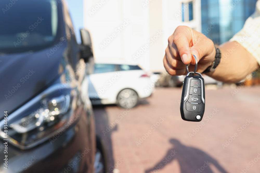 A hand near the car holds an electronic key, close-up