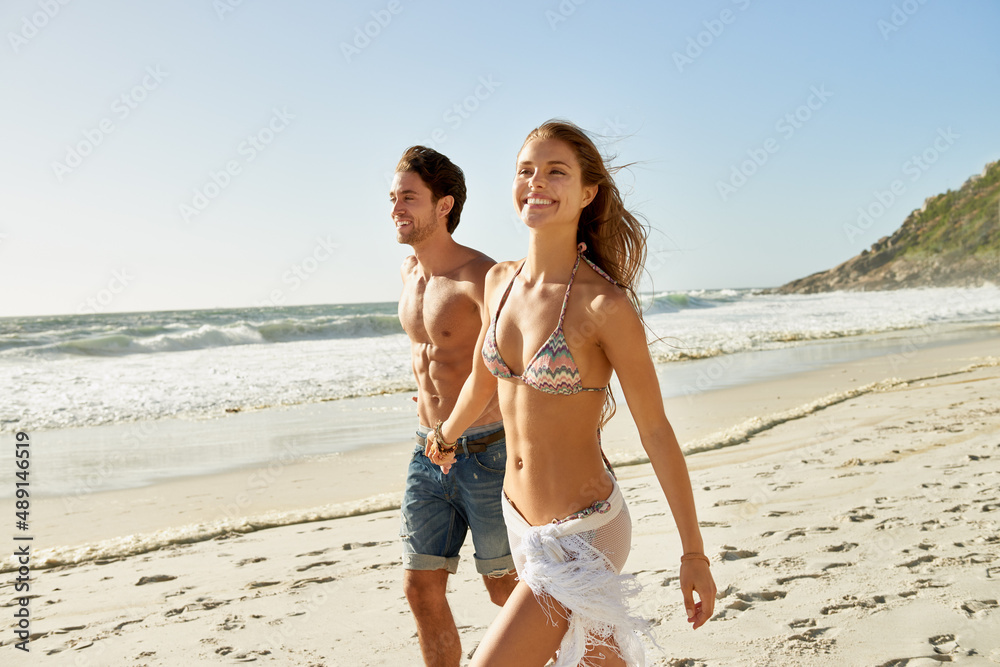 Happy days at the beach. Shot of a romantic young couple walking hand in hand on the beach. Happy days at the beach. Shot of a romantic young couple walking hand in hand on the beach.