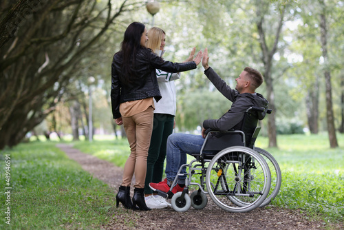 Young womens high five to men on a wheelchair in the park