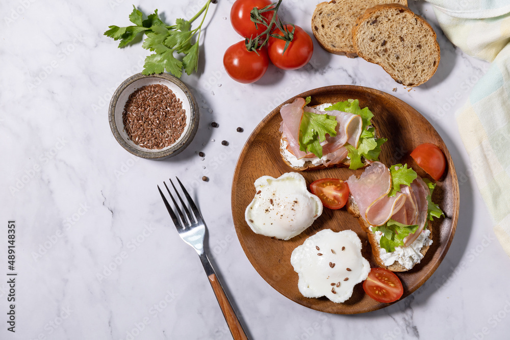 Easter breakfast or brunch. Delicious breakfast or snack - poached egg and cream cheese toast whole grain rye bread, prosciutto, arugula on a marble tabletop. Top view flat lay. Copy space. Easter breakfast or brunch. Delicious breakfast or snack - poached egg and cream cheese toast whole grain rye bread, prosciutto, arugula on a marble tabletop. Top view flat lay. Copy space.