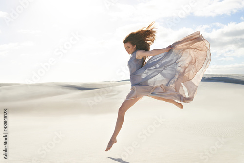 Freedom and isolation on the beach. Side view of a beautiful young woman in a flowing dress jumping across sand.