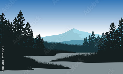 The magnificent view of the mountains with the silhouette of the pine trees from the lakeside on a foggy morning