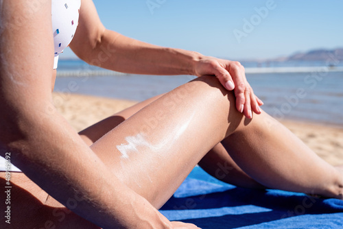 Sun protection cosmetics. Caucasian woman applying sun cream sunbathing on beach