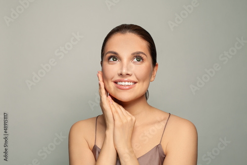 Smiling young woman touching her cheek smiling looking up over grey background