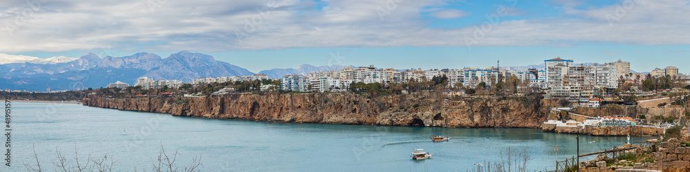 panorama of the coast of Antalya with a huge number of five-star hotels, palm trees, promenade, with boats sailing in the sea and mountains in the background