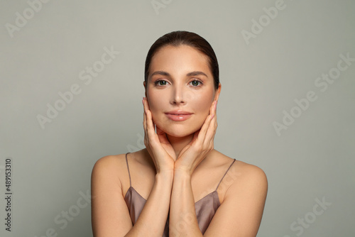 Beautiful spa model touching fresh glowing hydrated facial skin on gray background. Skin care concept