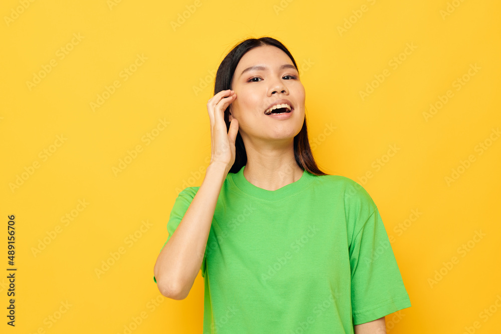 woman with Asian appearance in green t-shirts gestures with his hands emotions yellow background unaltered woman with Asian appearance in green t-shirts gestures with his hands emotions yellow background unaltered