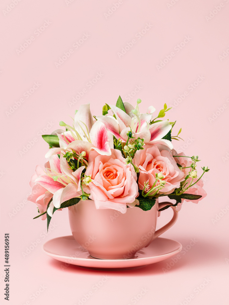 Tea cup filled with bouquet of fresh roses and orchids on pastel pink background. Creative floral spring bloom concept. Morning drink or healthy breakfast idea. Still life natural visual trend.