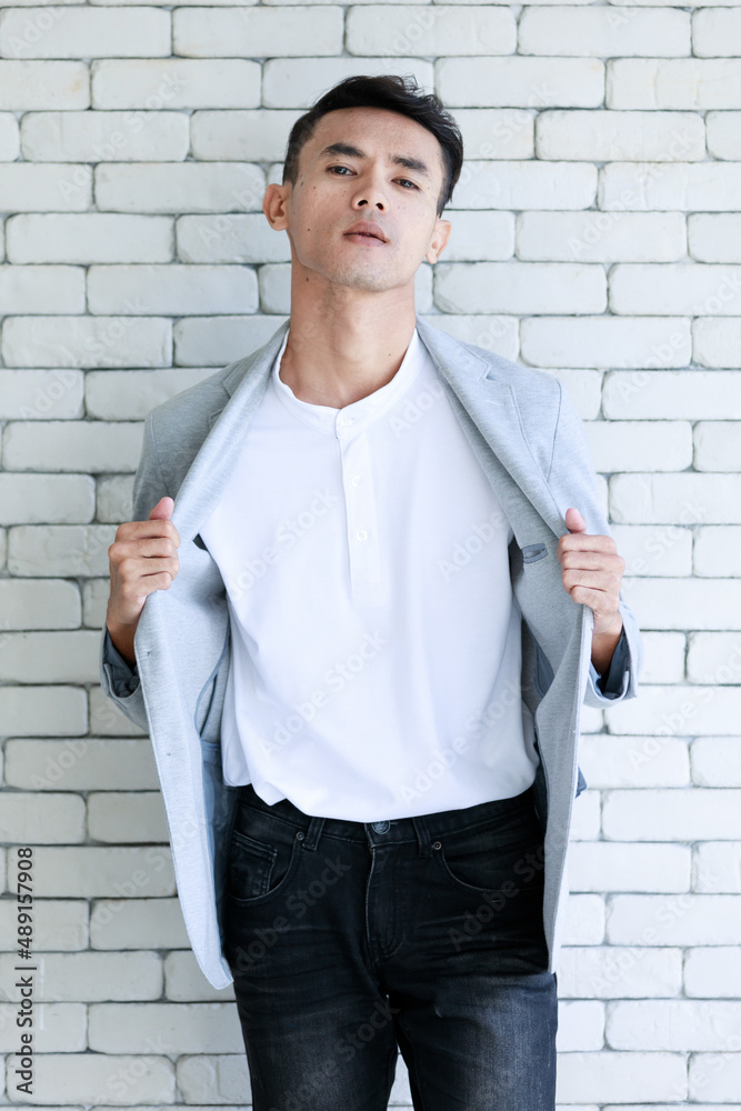 Portrait shot Asian young cool smart handsome muscular undercut hairstyle  male businessman in casual gray suit jacket standing holding hands in jeans  pockets look at camera on brick wall background Stock Photo |