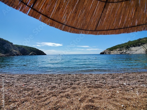 View of the open sea under a straw parasol on Queen s Beach in Montenegro.