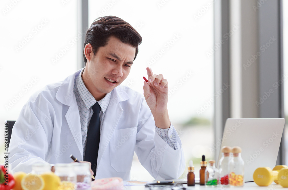 Portrait studio shot Asian male professional nutritionist dietitian doctor in white lab coat and stethoscope sitting holding pen smiling at working desk full of fruits vegetable nutrition supplements Portrait studio shot Asian male professional nutritionist dietitian doctor in white lab coat and stethoscope sitting holding pen smiling at working desk full of fruits vegetable nutrition supplements
