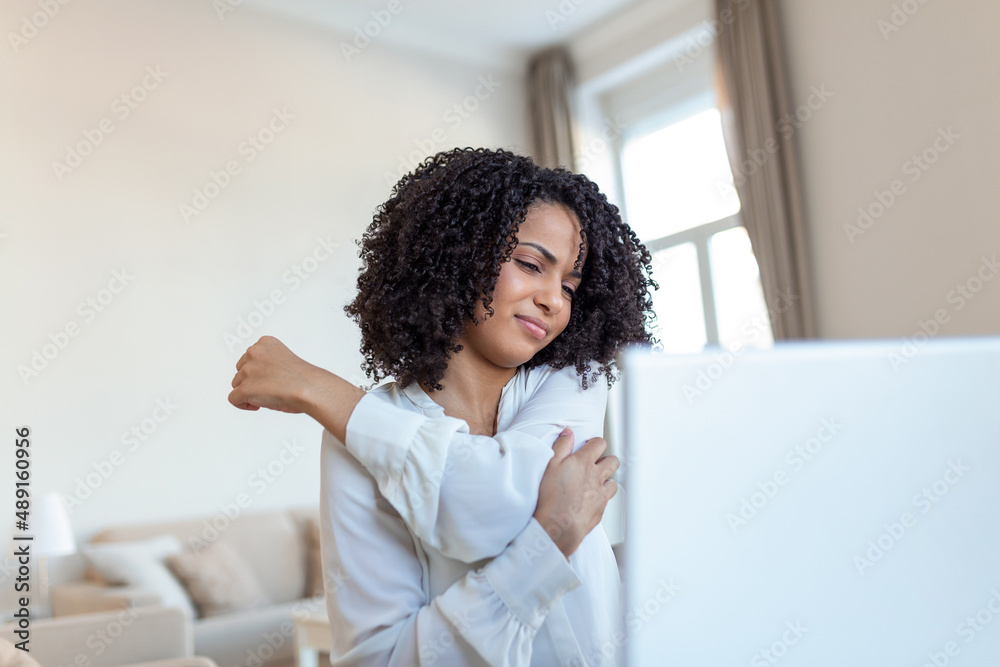 Portrait of young stressed woman sitting at home office desk in front of laptop, touching aching back with pained expression, suffering from backache after working on pc Portrait of young stressed woman sitting at home office desk in front of laptop, touching aching back with pained expression, suffering from backache after working on pc