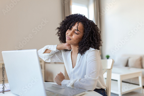 Feeling exhausted. Frustrated young woman looking exhausted and massaging her neck while sitting at her working place