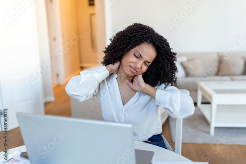 Businesswoman feeling pain in neck after sitting at the table with laptop. Tired female suffering of office syndrome because of long hours computer work. Pretty girl massaging her tense neck muscles