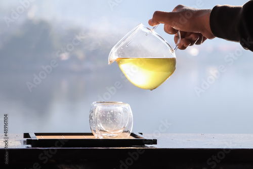 Female hands pouring hot tea with lake background at sunrise.