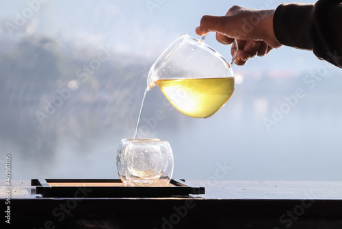 Female hands pouring hot tea with lake background at sunrise.