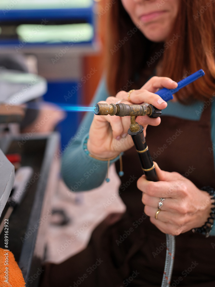 a woman working in her artisan jewelry workshop adjusting a torch to perform her work.