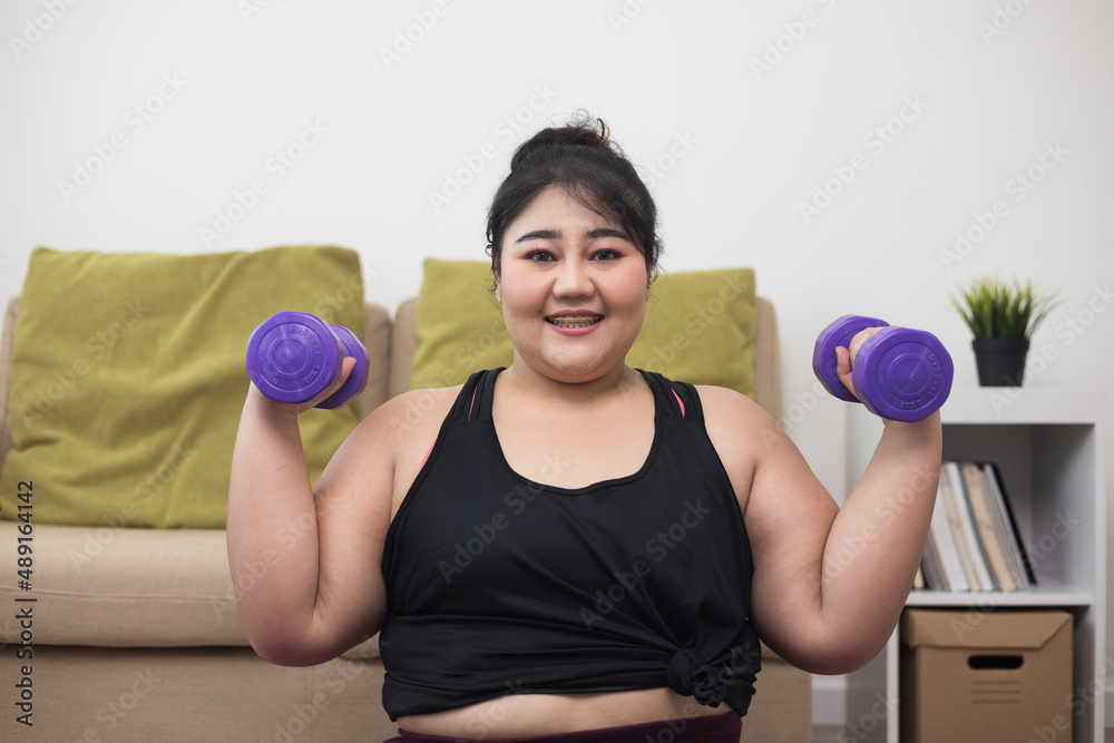 Attractive asian young fitness woman plus size lifting dumbbell weights workout at home in living room. Fresh feeling female training and exercise wearing sport wear fit body. Attractive asian young fitness woman plus size lifting dumbbell weights workout at home in living room. Fresh feeling female training and exercise wearing sport wear fit body.