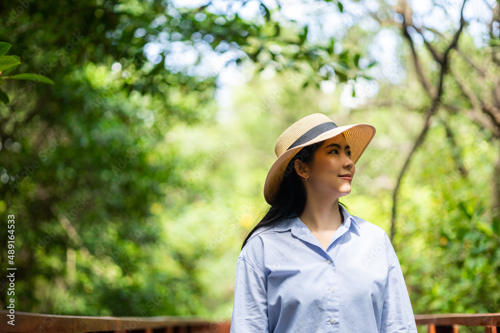 Young asian woman travel in the middle of nature with sunlight. Traveller blogger in mangrove forest. Rest on vacation holiday weekend. Beautiful female with hat and blue shirt walking in forest