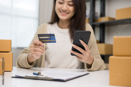 Shopping online. Young asian woman input the serial number of credit card to smartphone for shopping payment. Buying online at home. Small business entrepreneur with many parcel box on table